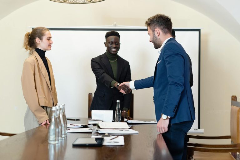 A diverse group of business professionals in a meeting room, shaking hands as a sign of agreement.